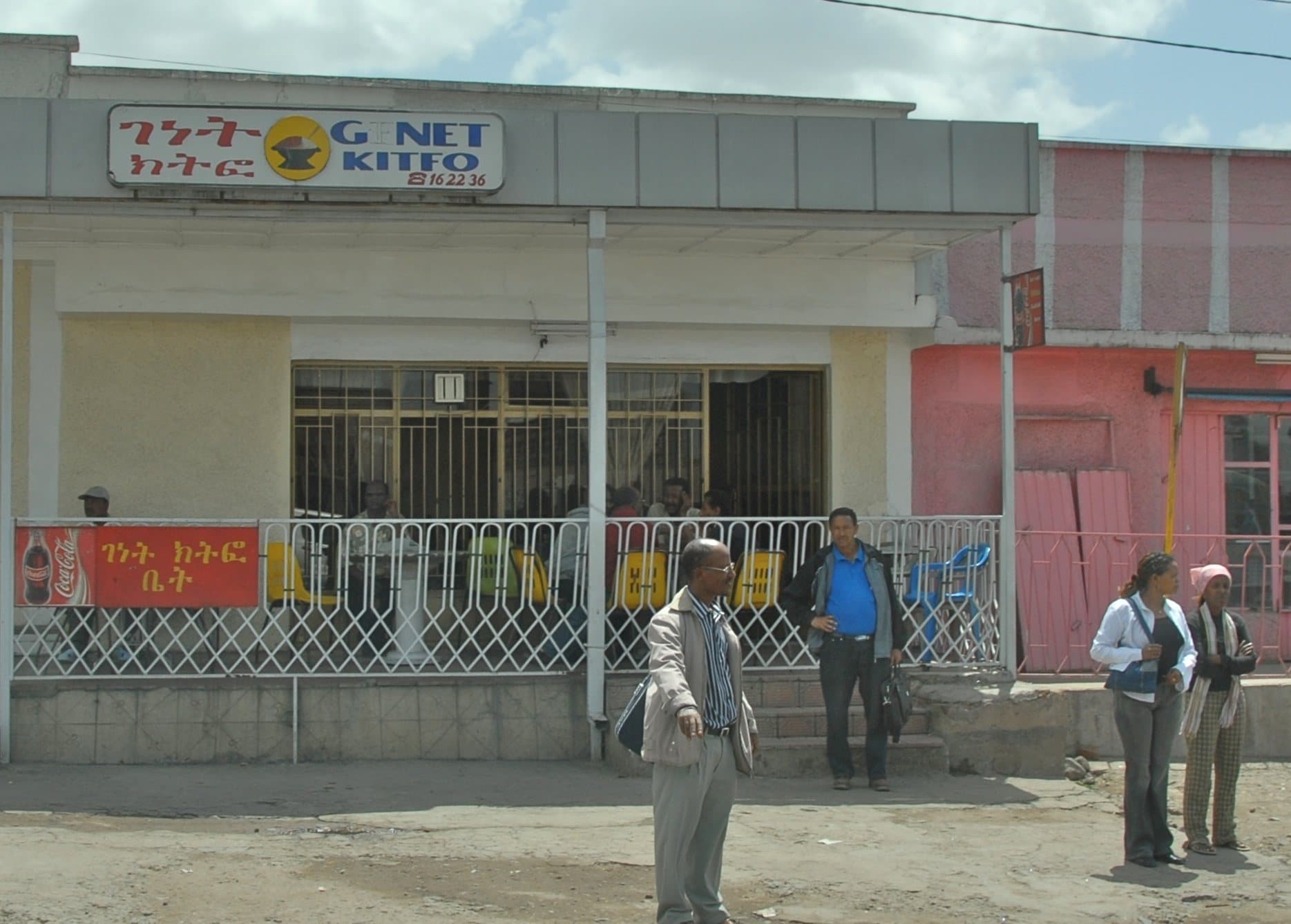 A kitfo house on a street in Ethiopia, with its sign in Amharic and English and people standing outside