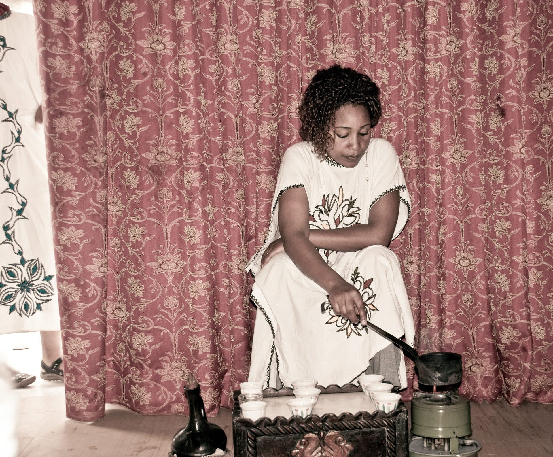 A young woman in a white habesha qemis roasting coffee beans for a coffee ceremony in Addis Ababa