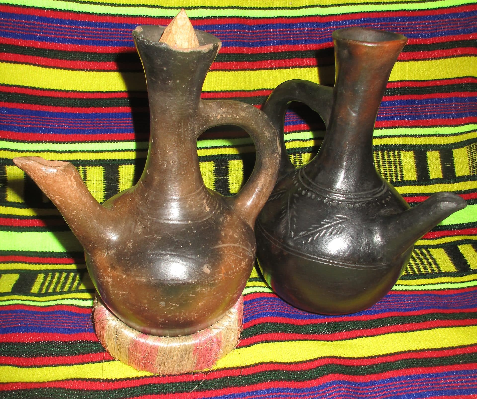 Two black clay jebena coffee pots on a striped woven cloth