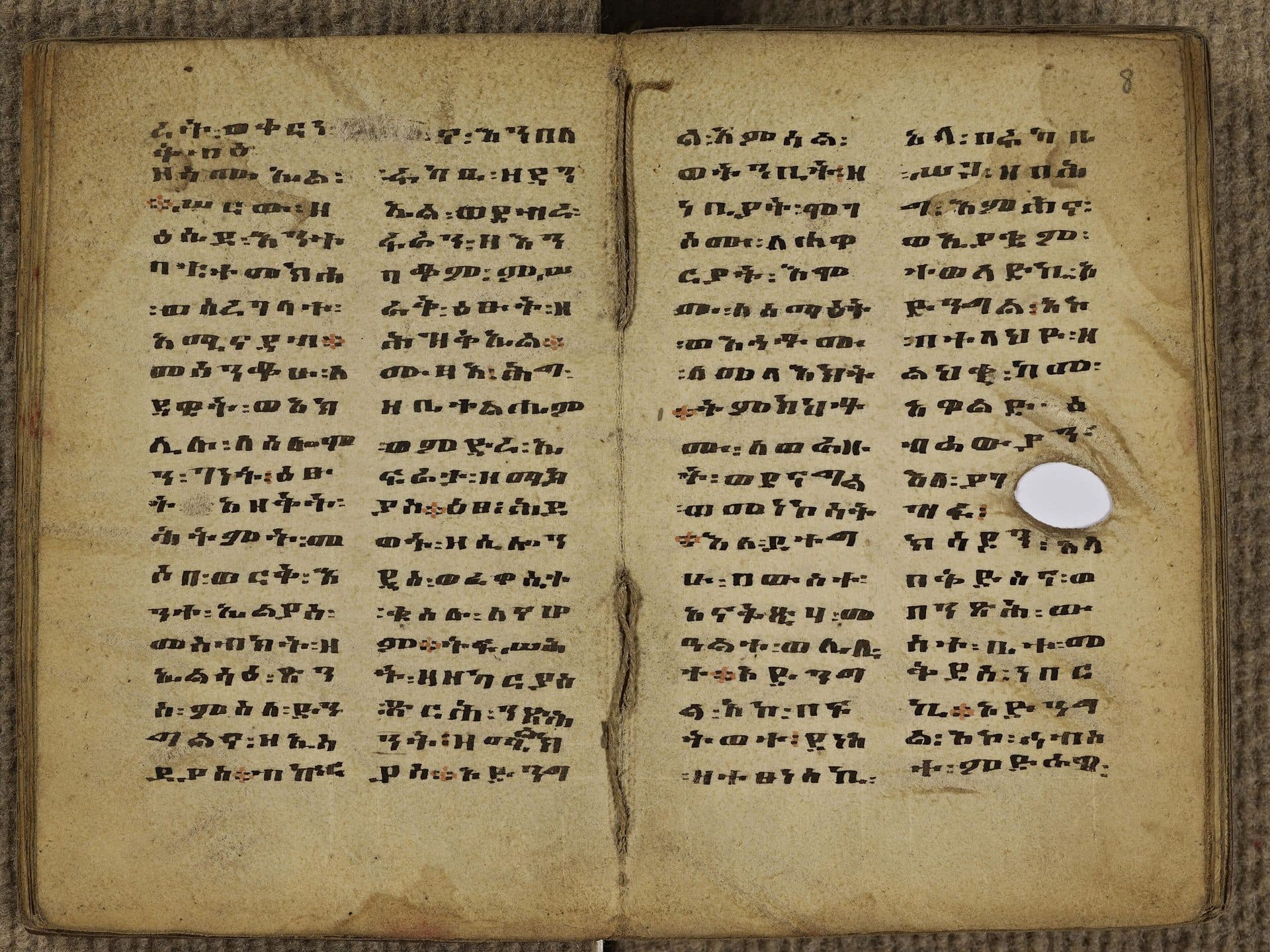 An open handwritten Ethiopian manuscript with columns of black and red Ge'ez script on worn parchment