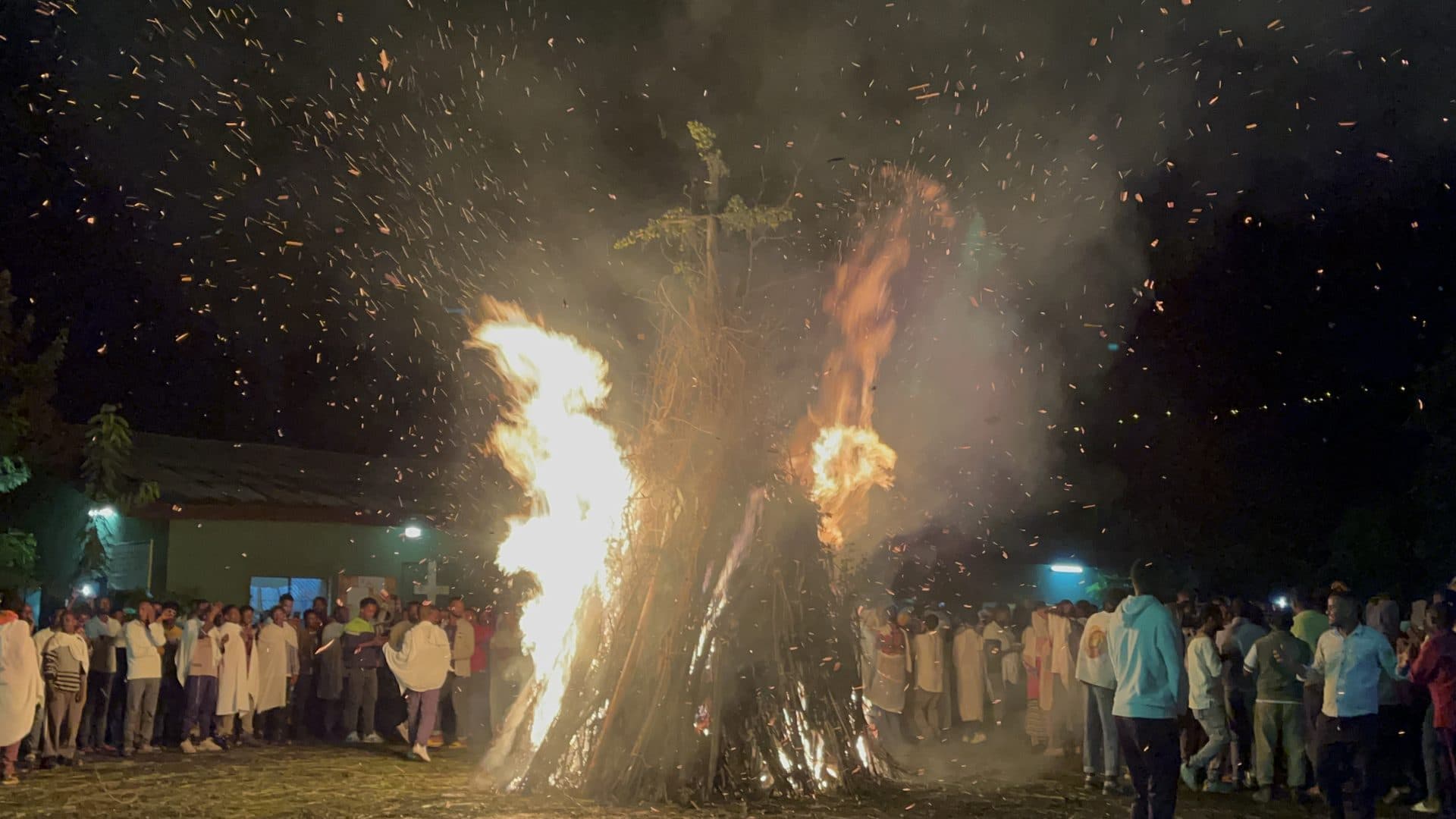 Tall Meskel bonfires blazing at night with sparks rising over a large crowd