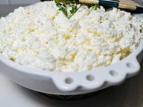 A white bowl of fresh, crumbly ayib cheese topped with a few green herbs