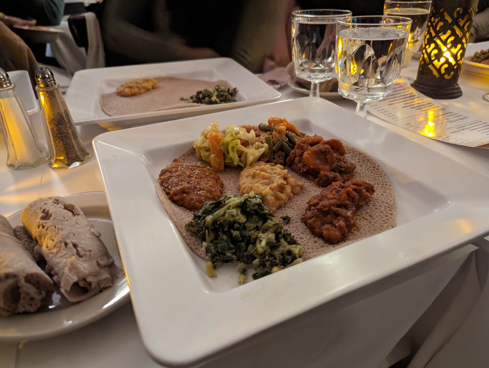 A vegetarian sampler of lentils, split peas, greens and vegetables on injera, with rolled injera alongside