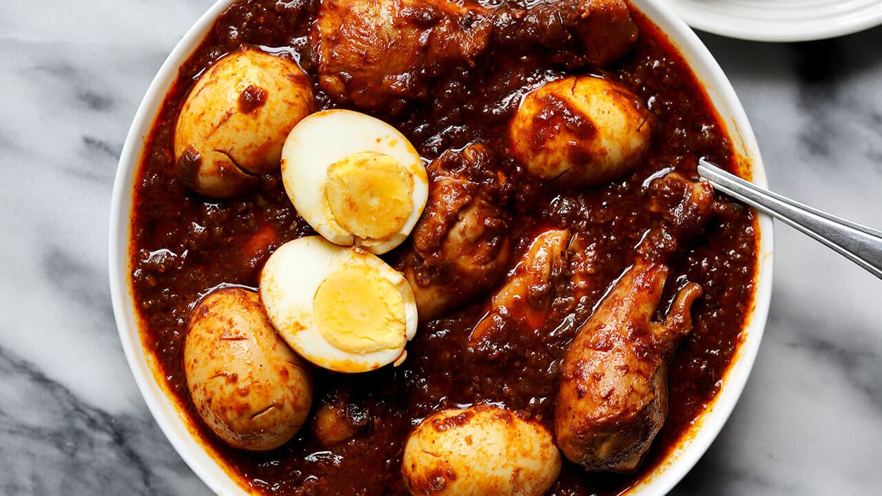 A bowl of doro wat: chicken pieces and hard-boiled eggs in a deep red berbere sauce