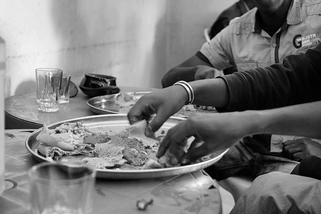 Hands tearing injera and scooping from a shared metal tray in Ethiopia