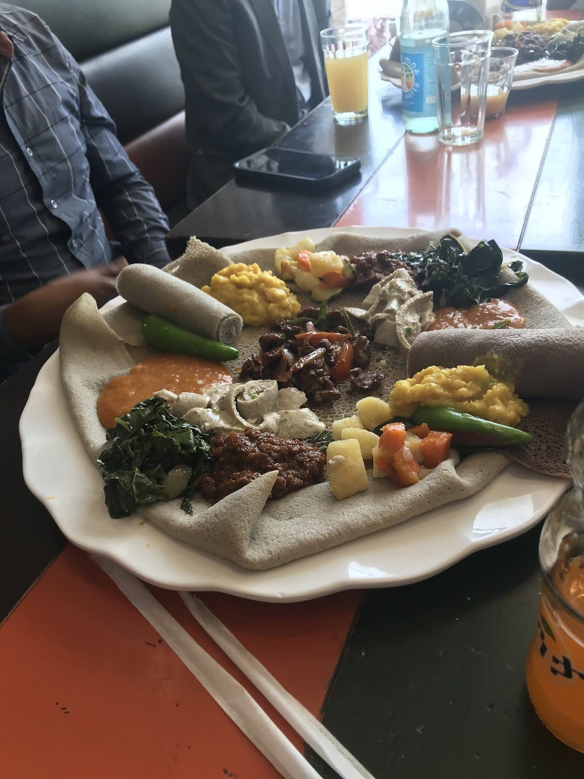 A right hand tearing a piece of injera over a platter of lentils, greens and vegetables