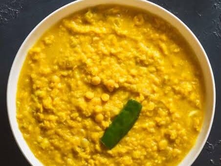 A white bowl of yellow split pea kik alicha with a green chili on top