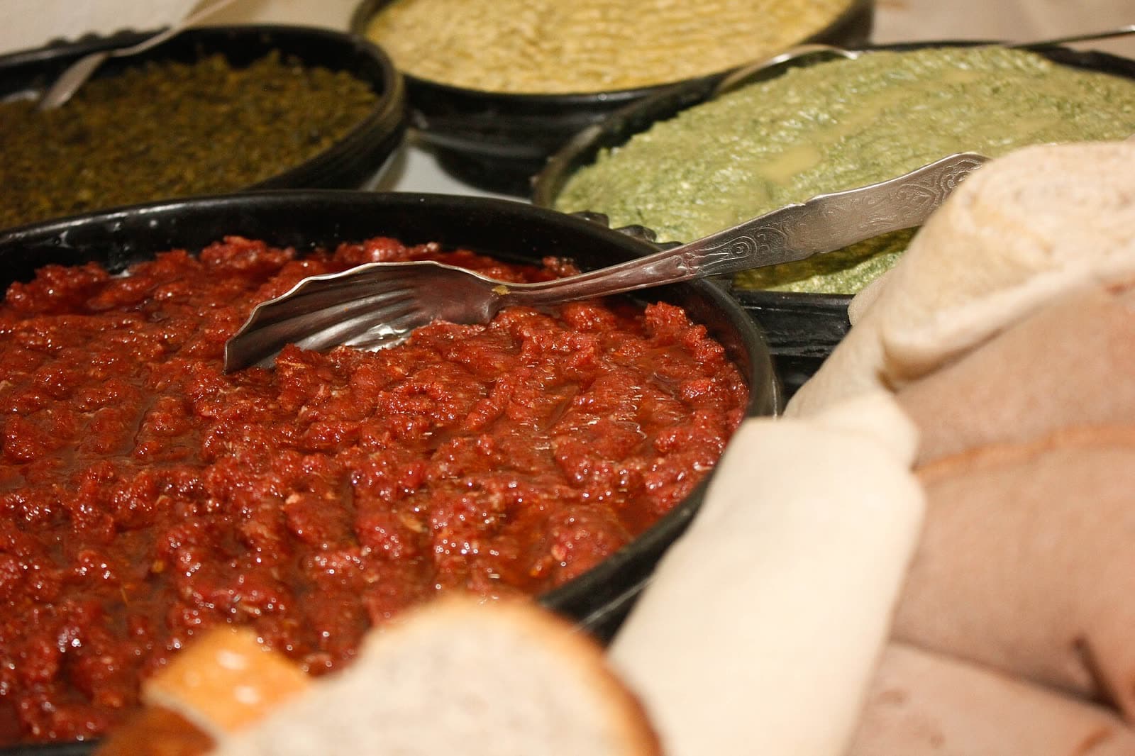 A bowl of red, spiced minced kitfo beside a dish of white ayib cheese and folded injera