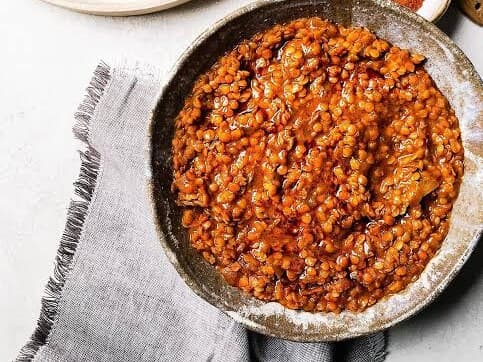 A rustic bowl of red lentils in a deep orange berbere sauce, on a gray linen cloth