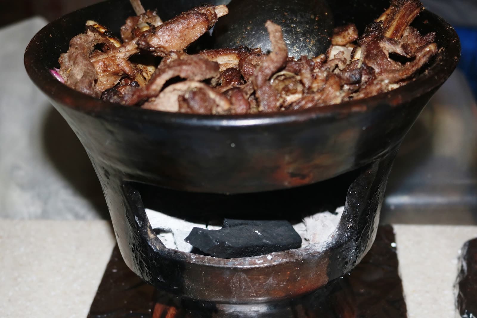 Shekla tibs sizzling in a black clay dish set over glowing charcoal