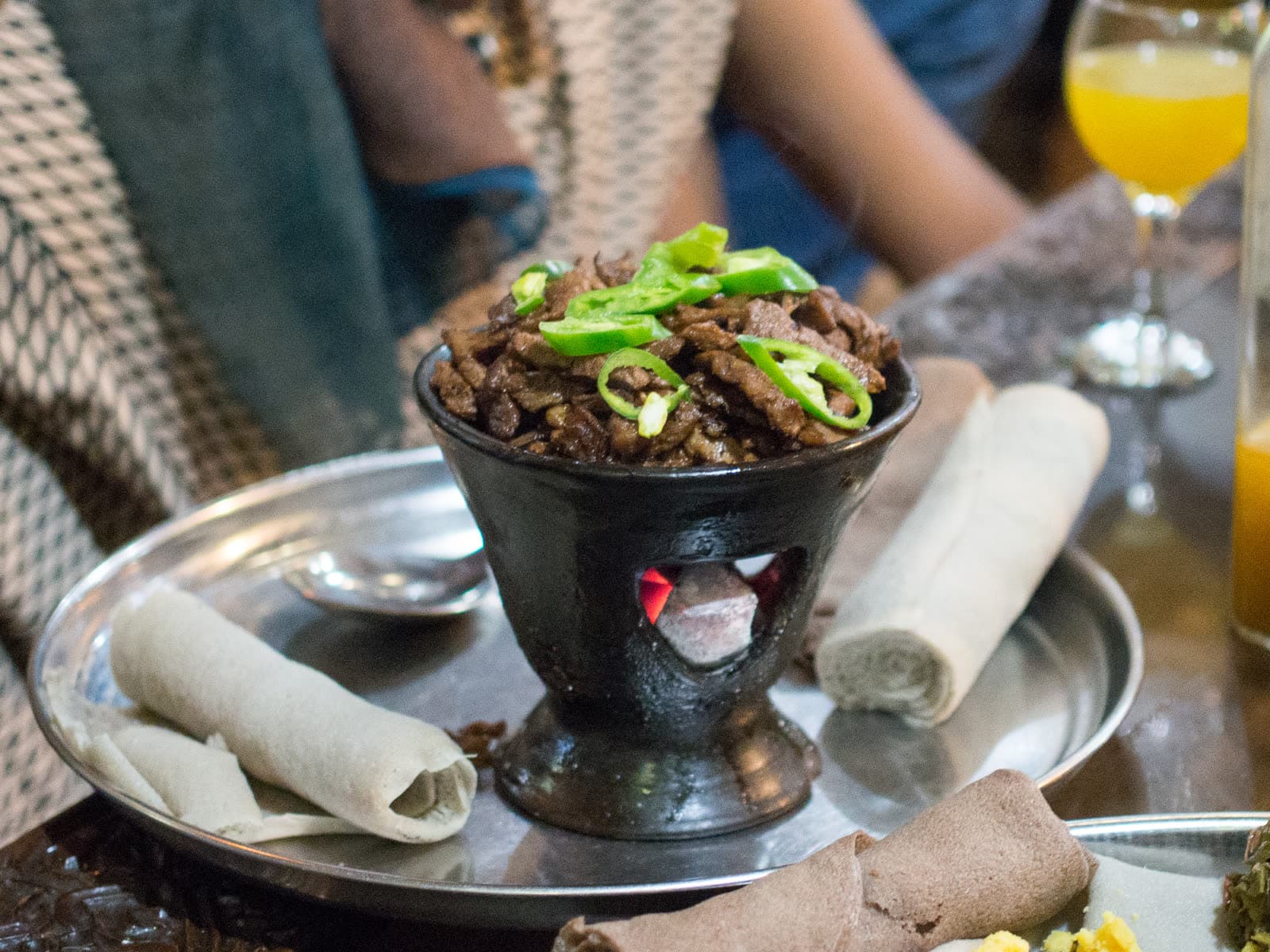 Tibs topped with sliced green peppers, served in a black clay dish on a tray with rolled injera