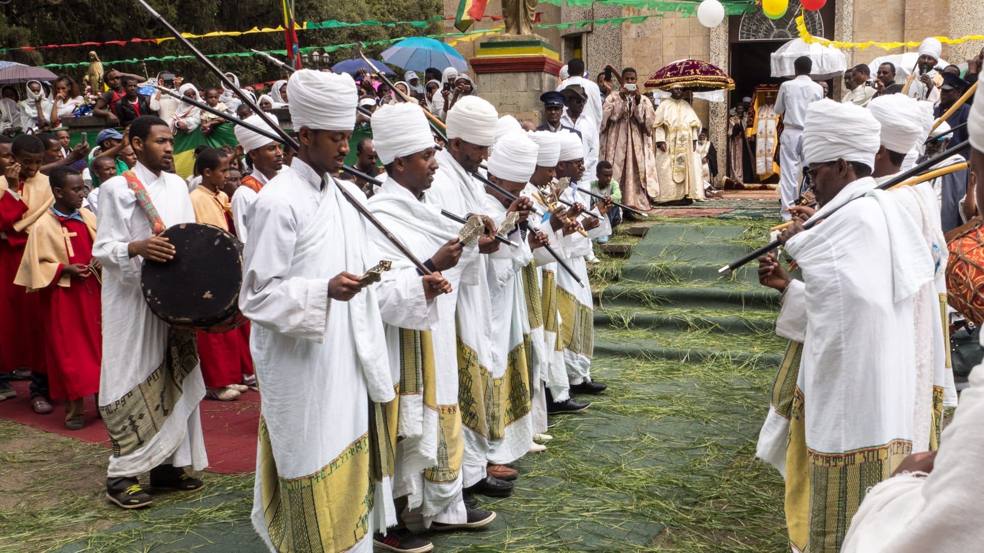 Ethiopian Orthodox priests in white robes and turbans dancing with prayer staffs and a drum during Timkat