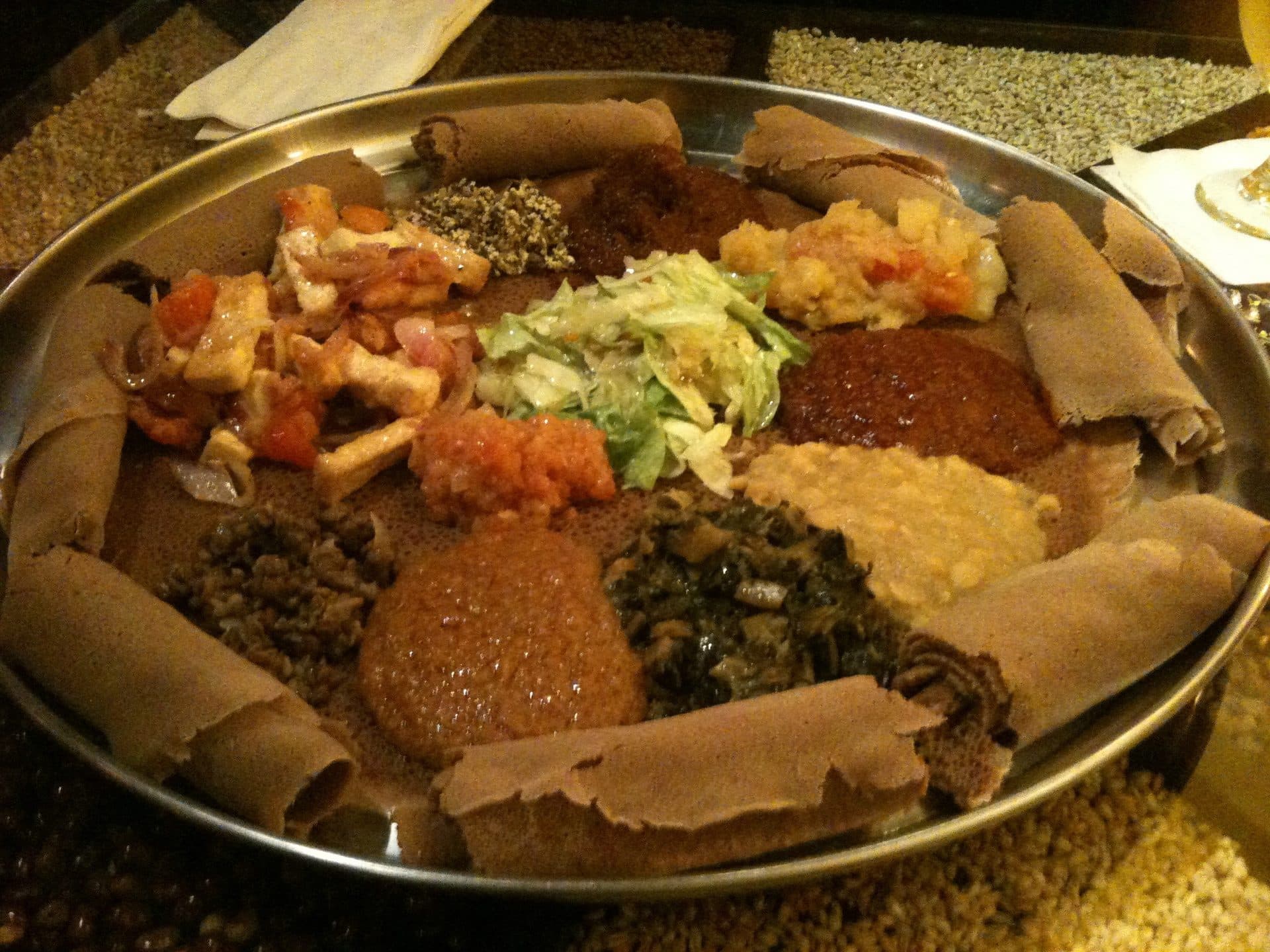 A large round of injera covered in a ring of vegetable stews, lentils, greens and salad