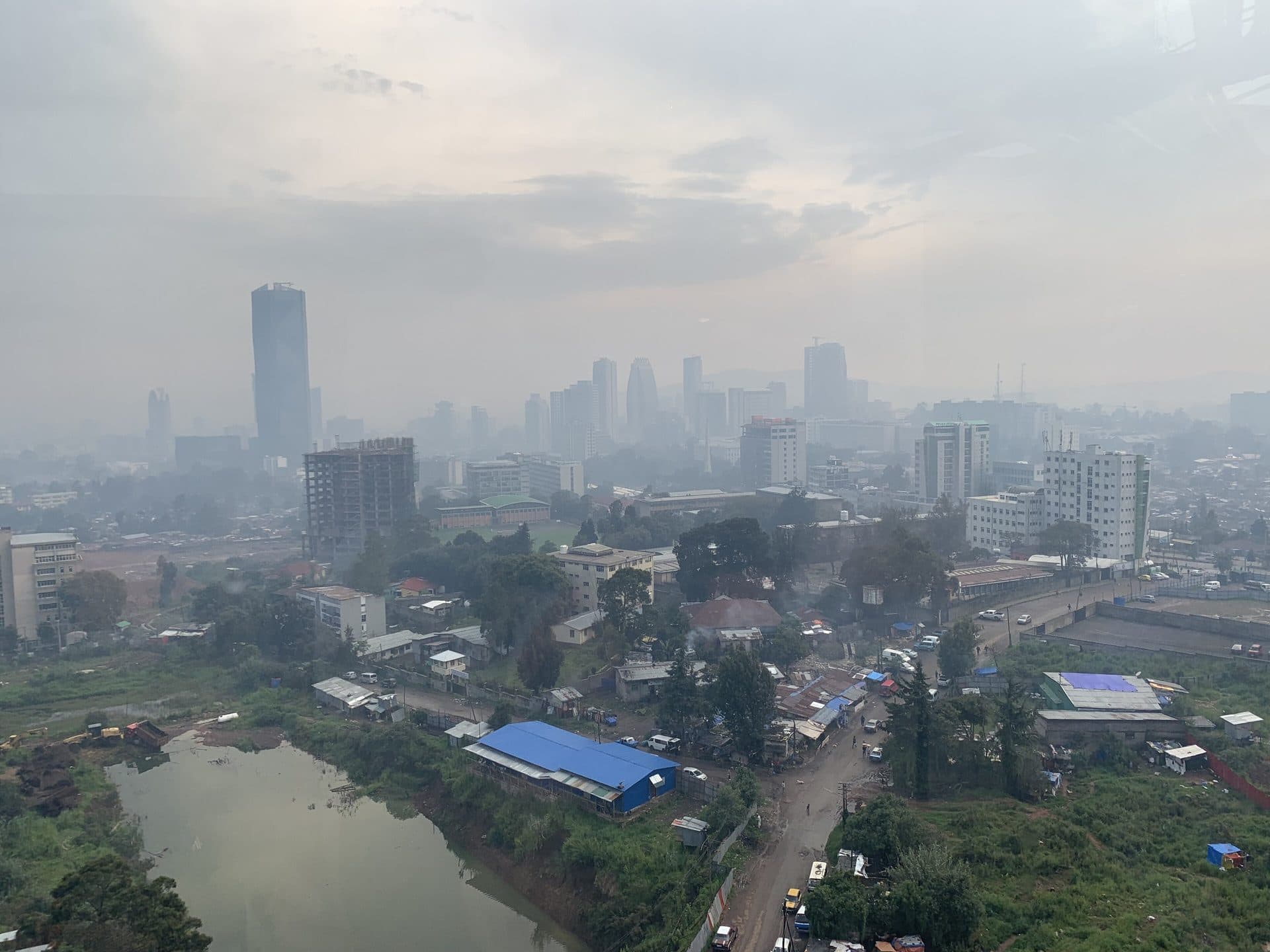 A wide view over Addis Ababa under grey rainy-season skies, with a pond and towers in the distance