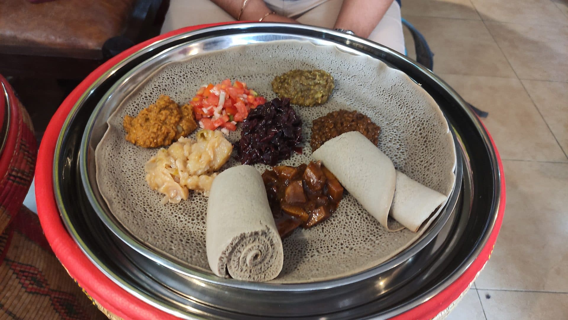 A beyaynetu platter of small mounds of vegetable stews on injera, with rolled injera on the side