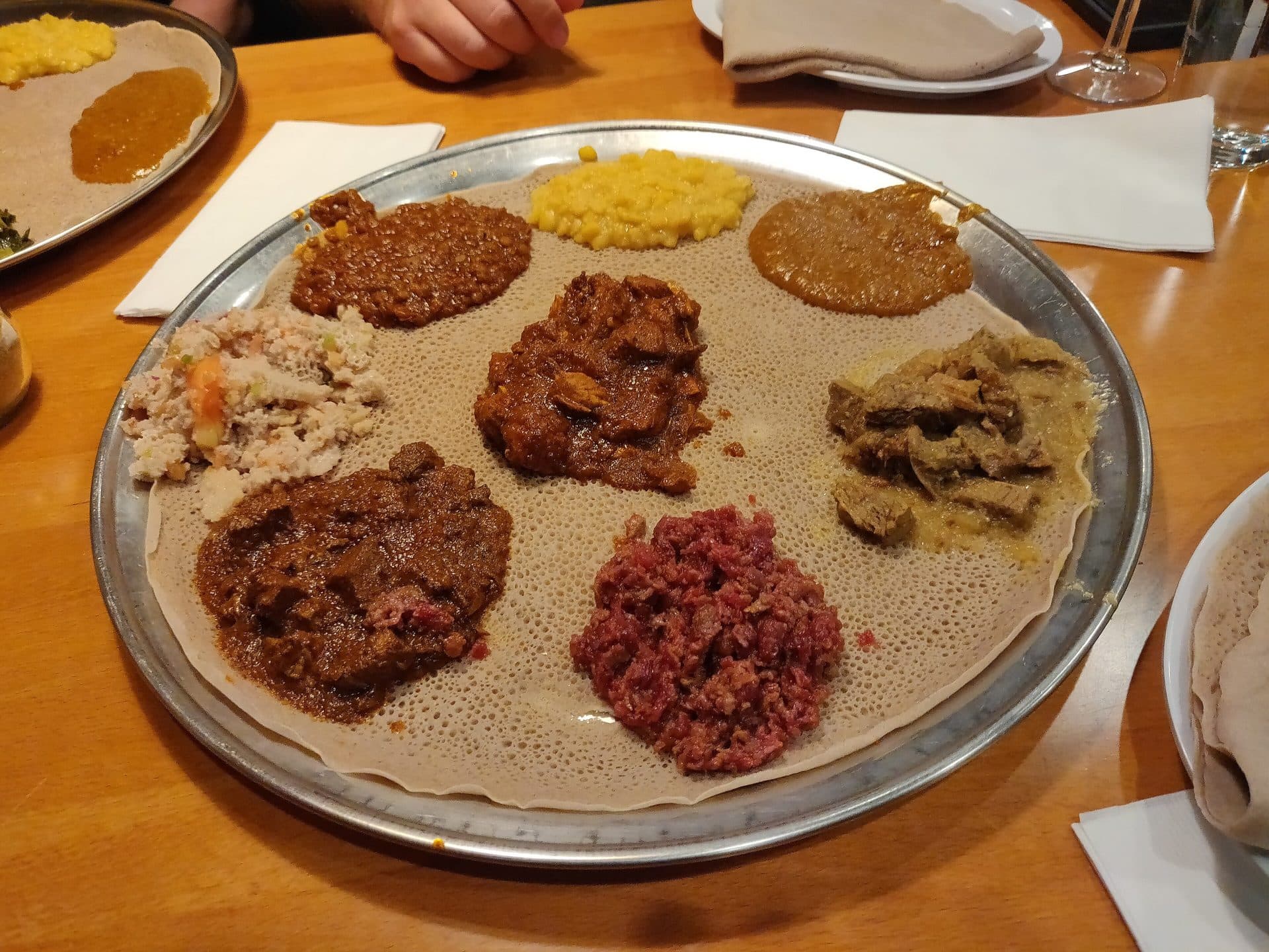 A large metal platter lined with injera and topped with several meat and vegetable dishes on a restaurant table