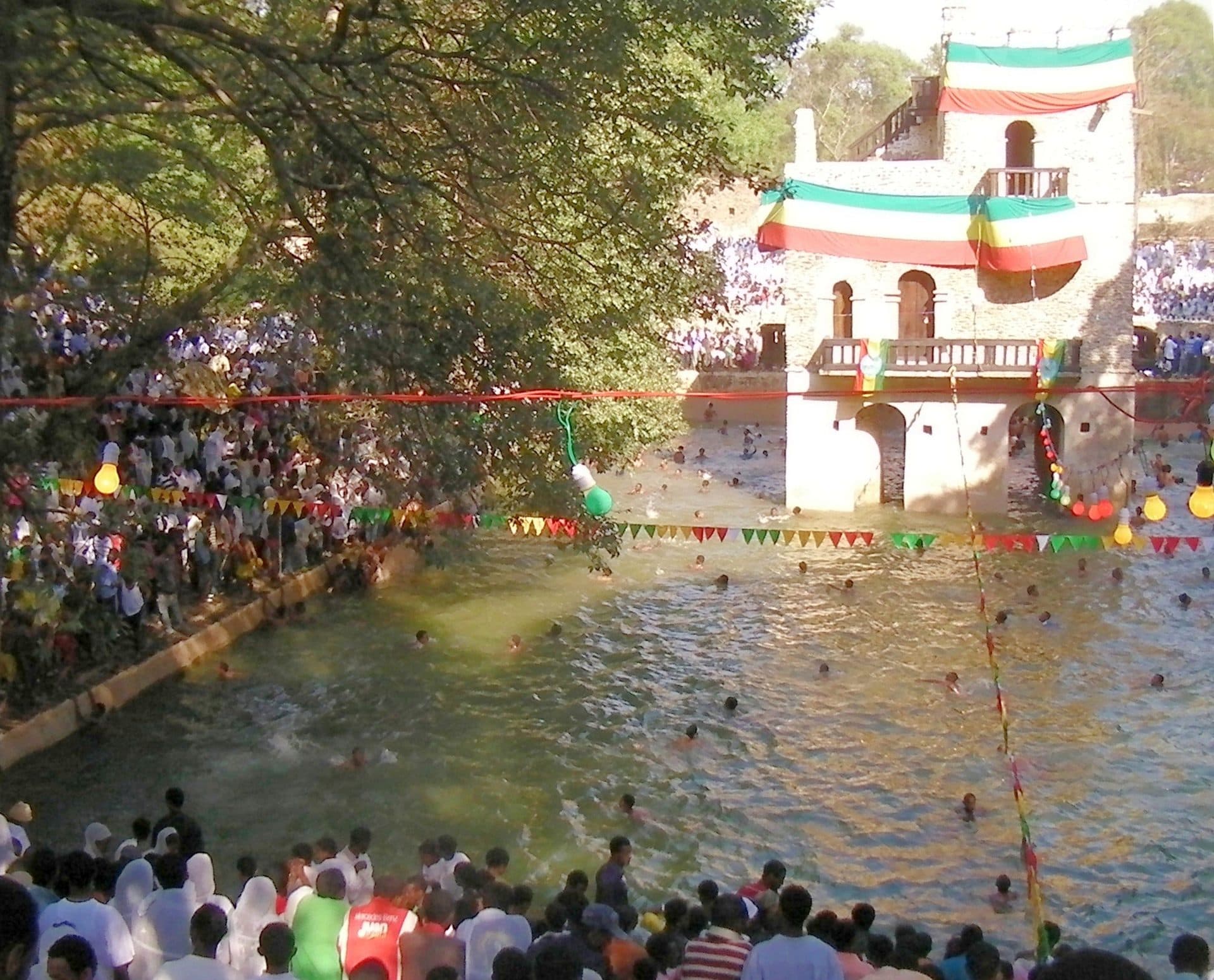 Crowds around the flag-draped pool of Fasilides' Bath in Gondar during Timket, with swimmers in the water