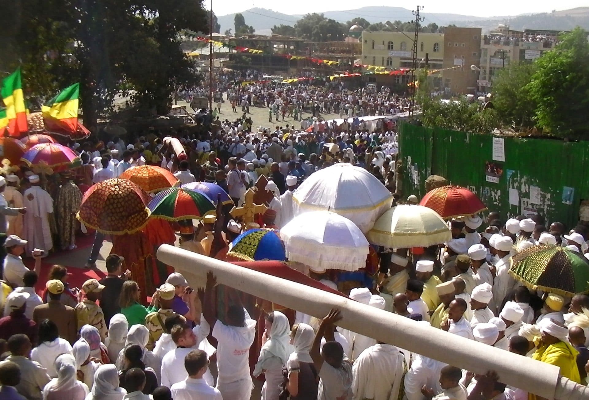 A huge crowd in white with colorful ceremonial umbrellas filling a street in Gondar