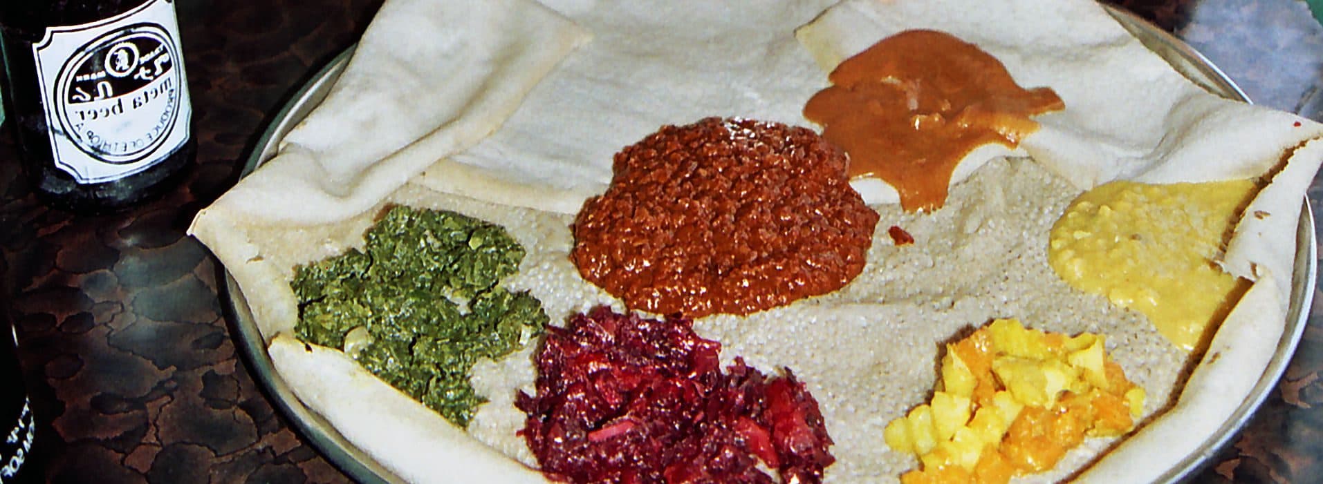 A round of injera topped with colorful vegetable dishes: lentils, greens, beets and potatoes