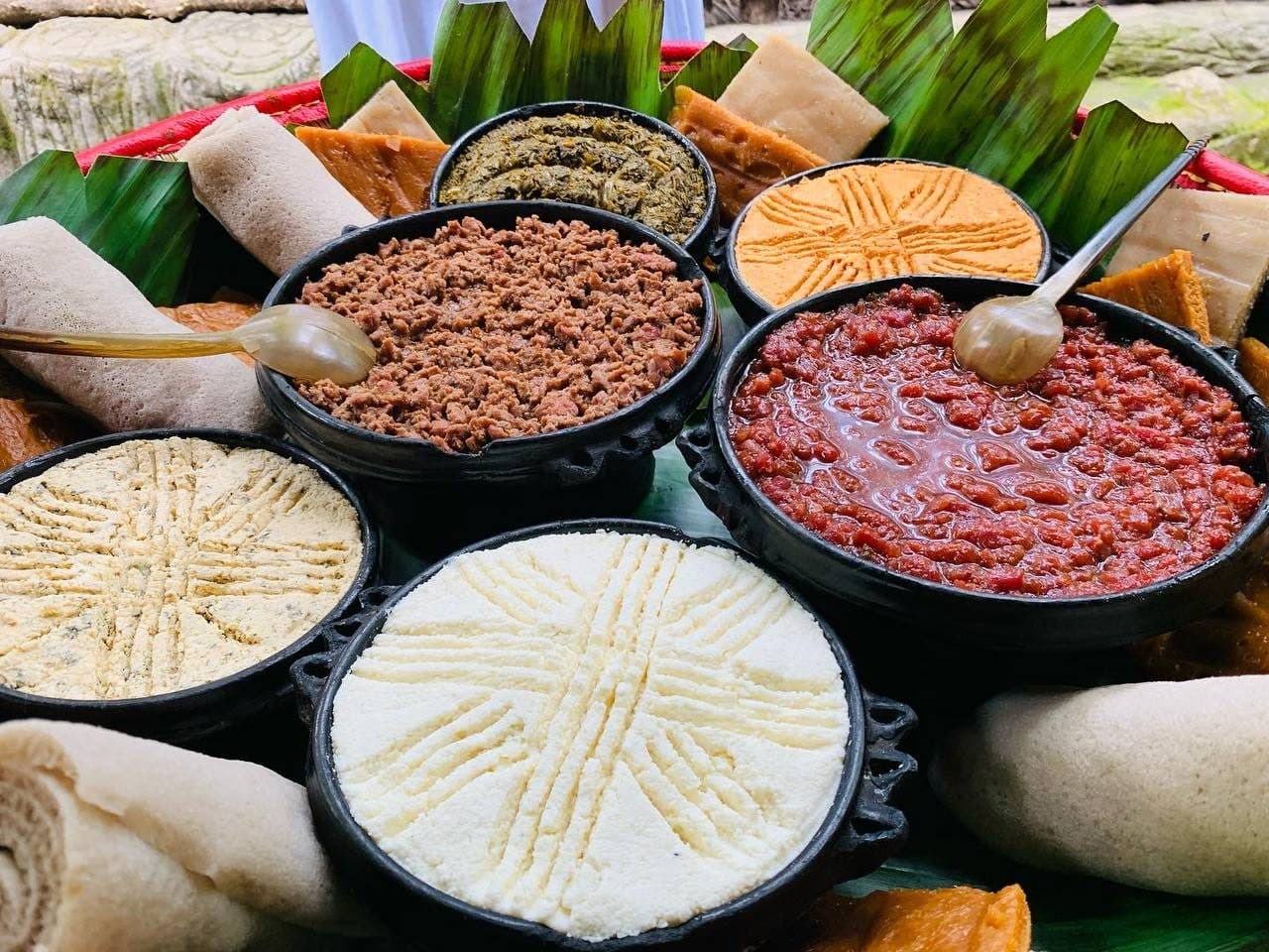 Bowls of minced kitfo, red sauce and fresh cheese laid out with rolls of injera