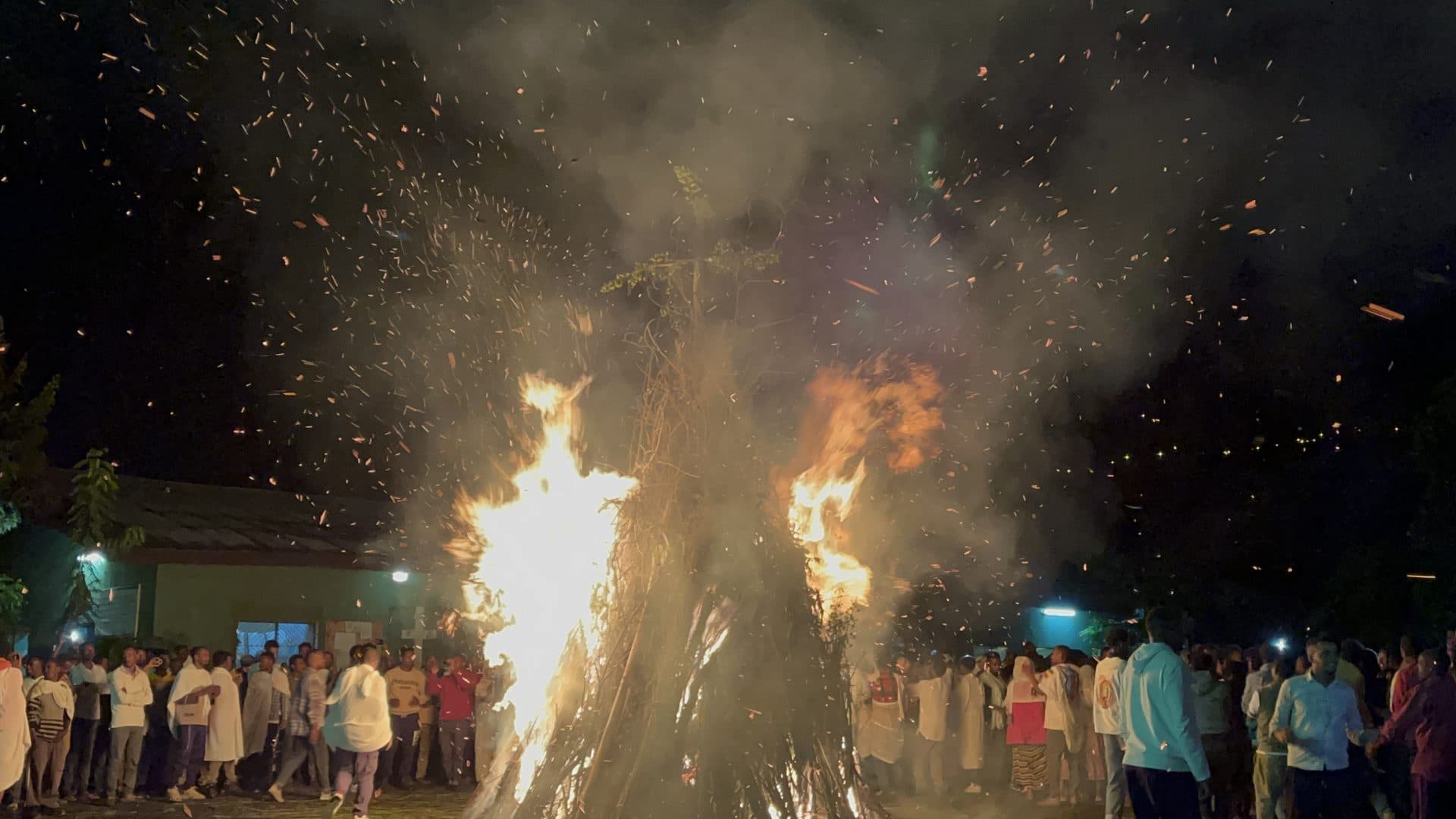 The Meskel demera bonfire burning at night, sparks rising over a crowd