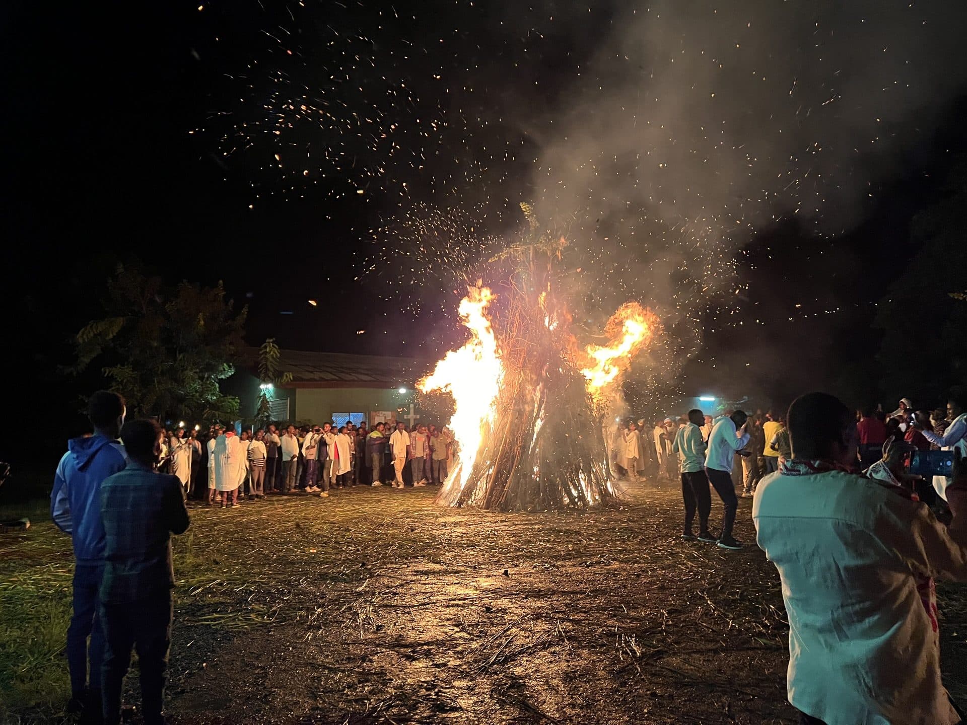 People gathered in a wide circle around a blazing Meskel bonfire at night