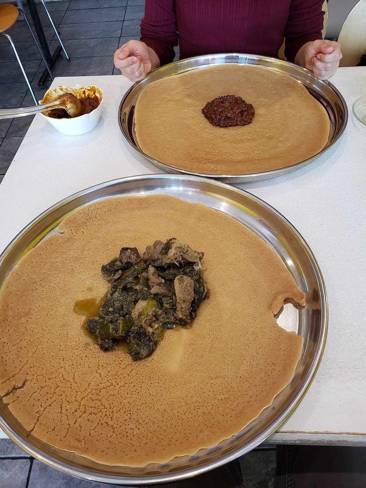 Two trays lined with injera, one topped with red lentil stew and one with collard greens